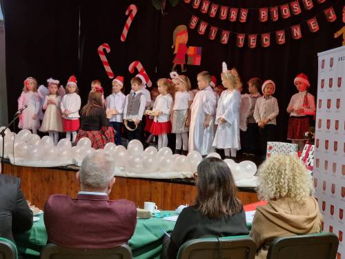 Grupa dzieci w strojach aniołków i czapkach Mikołajów na scenie